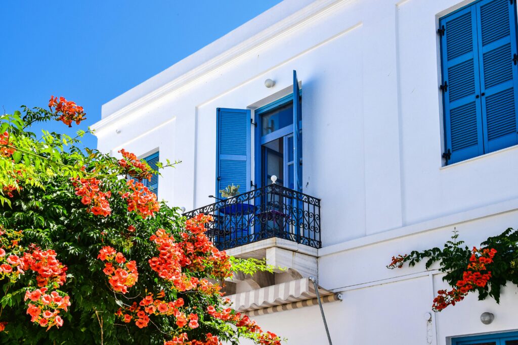 Beautiful white villa in Paros, Greece with blue shutters and vibrant orange flowers, capturing the essence of summer.