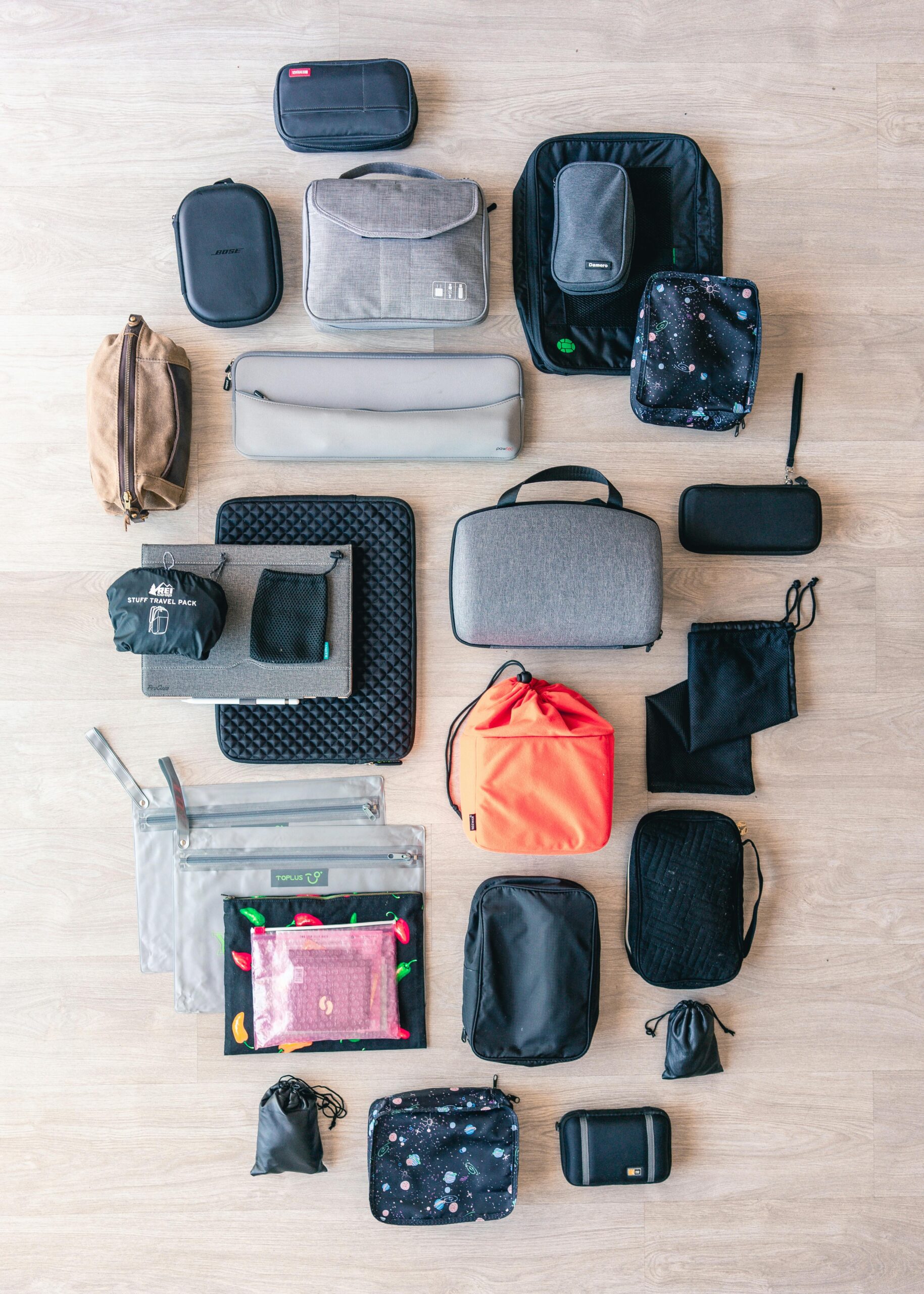 Flat lay of assorted travel bags and accessory pouches on a wooden floor.