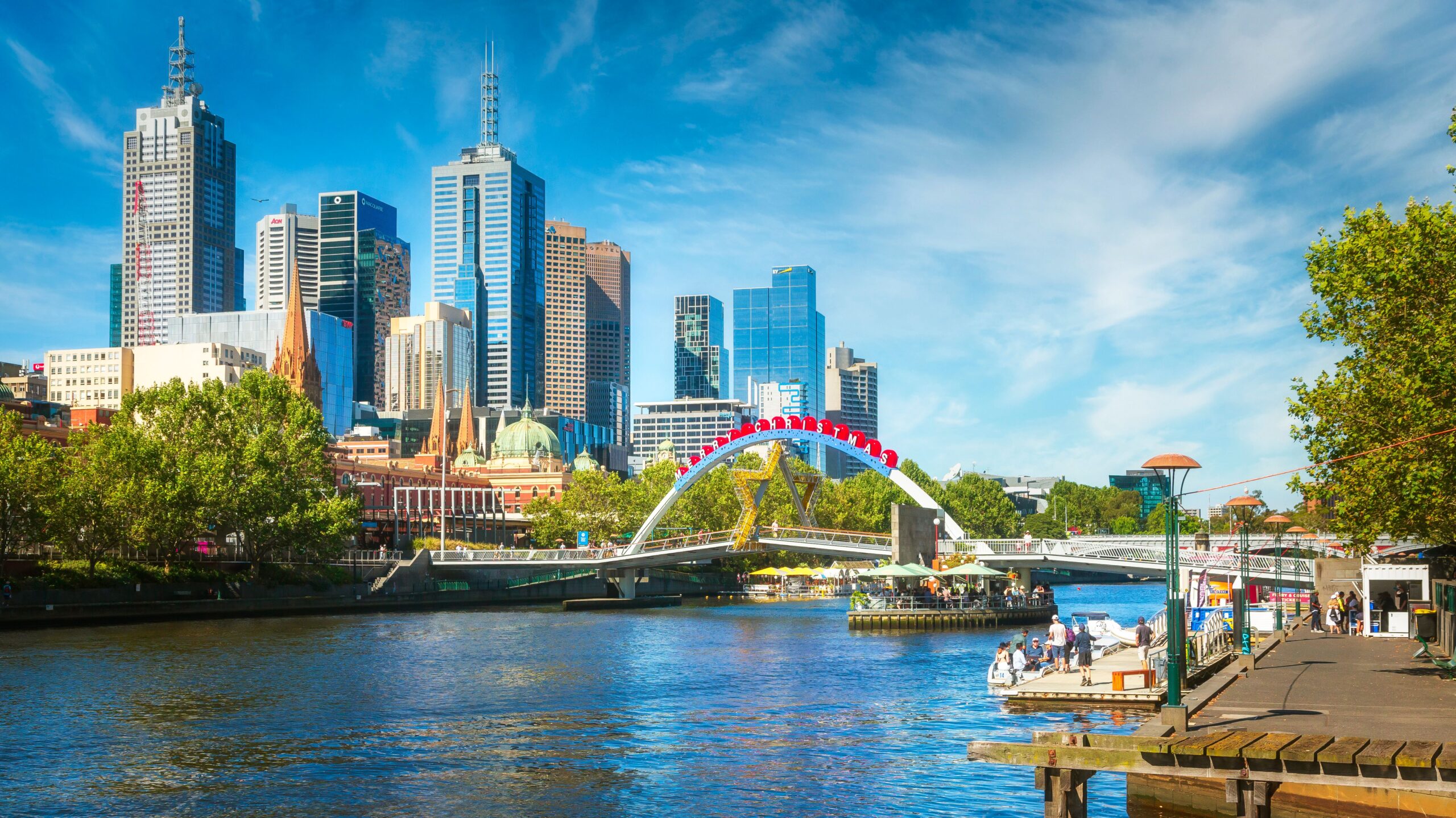 Scenic view of kayakers on Yarra River against Melbourne's modern skyline under a bright sky.